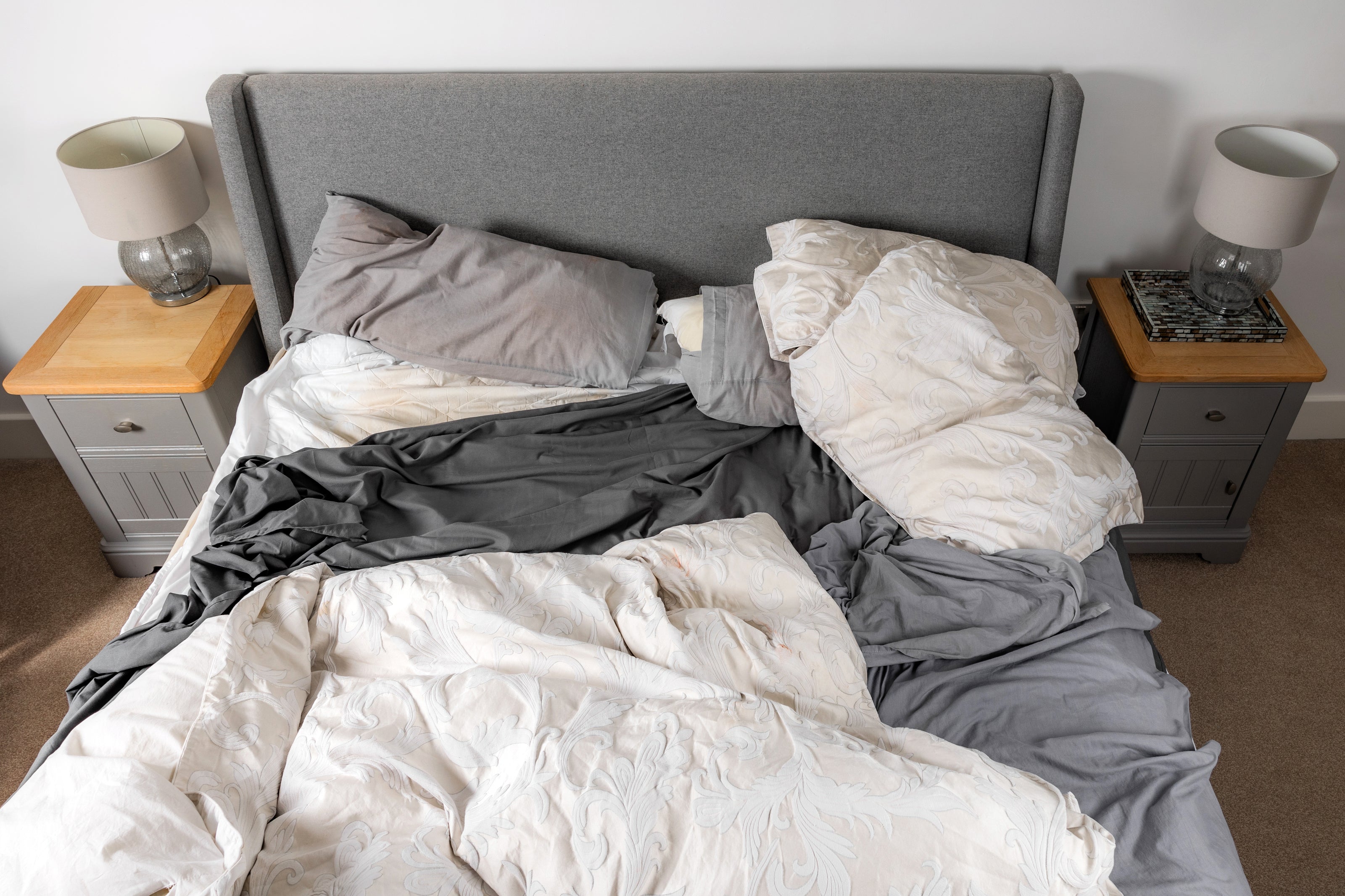 Unmade bed with gray and white bedding in a bedroom setting.